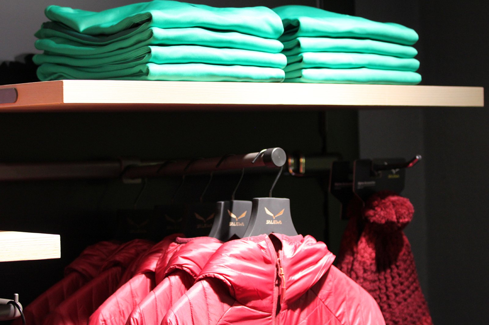Im Regal ein Stapel von grünen Shirts, darunter hängen rote Skijacken